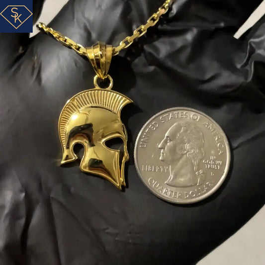 Gold Spartan helmet pendant next to a U.S. quarter dollar on black fabric